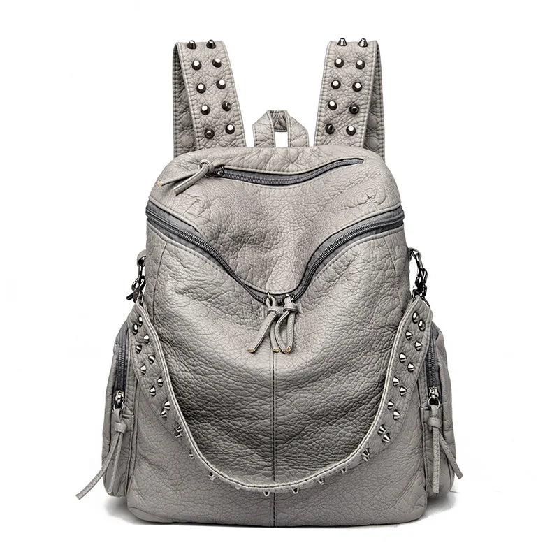 Sac à dos en cuir souple gris clair et rivetée avec plusieurs sangles et clous décoratifs.