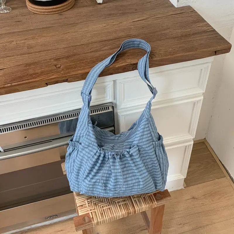 A light blue plaid nylon drawstring tote bag resting on a wooden block next to a kitchen counter.