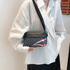 A woman holds a black and gray patterned square crossbody purse against a white striped shirt.