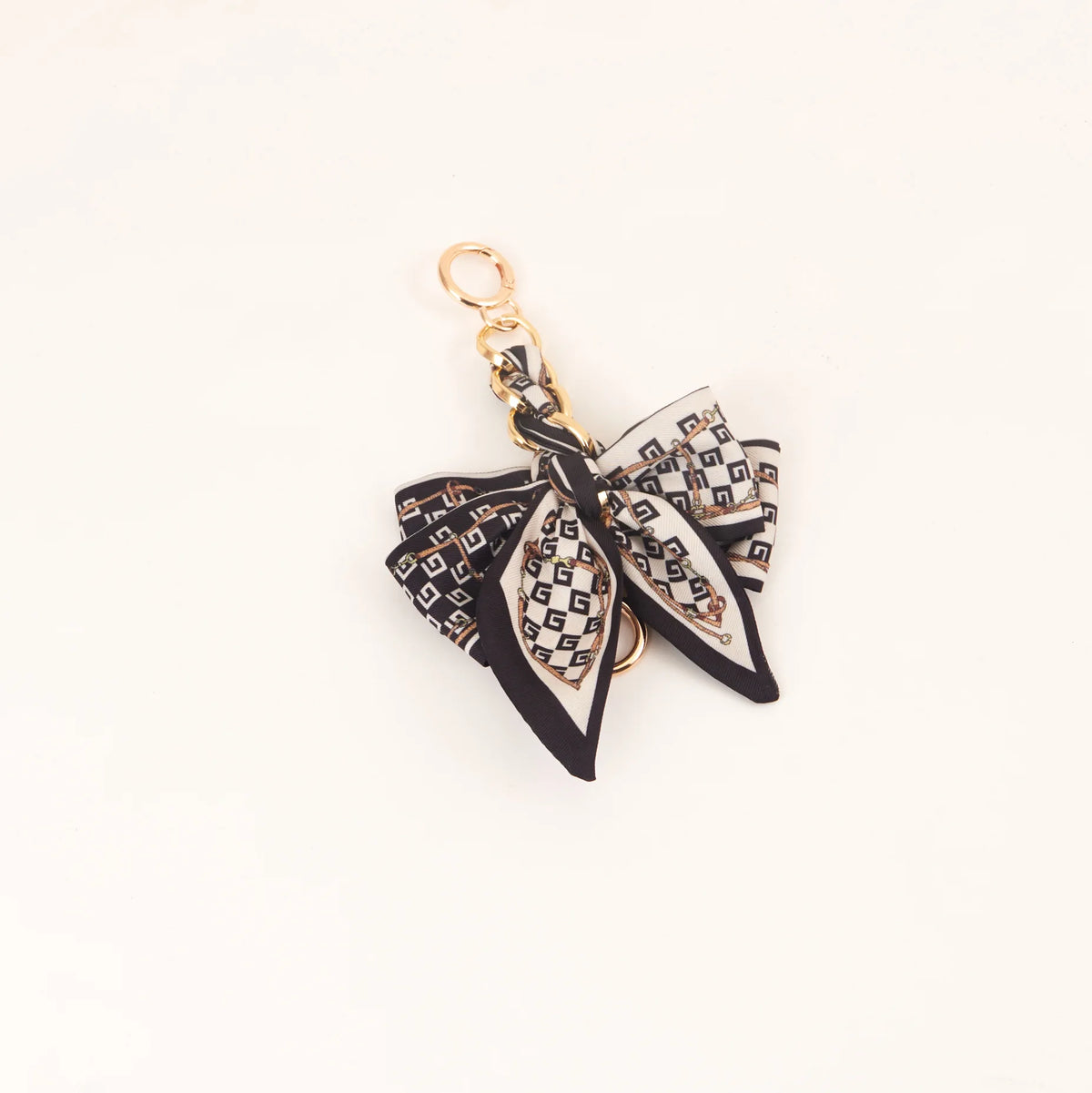 Llavero tono dorado con elegante lazo de cinta de seda y patrón geométrico blanco y negro.