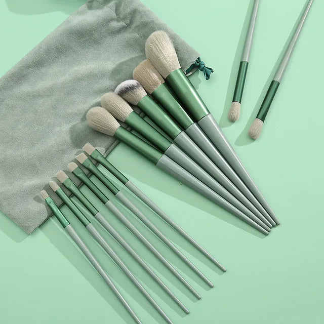 Una colección de trece brochas de maquillaje profesionales en varios tonos de verde y beige sobre una superficie verde claro.