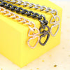 A collection of heart-shaped metal purse chains and extenders in gold, silver, and black lying on a yellow box.