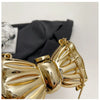 A close-up of a gold acrylic bow clasp mini handbag with a chain strap resting on a black fabric.