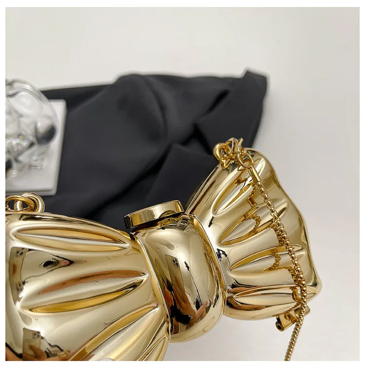 A close-up of a gold acrylic bow clasp mini handbag with a chain strap resting on a black fabric.