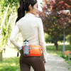 A woman wearing a beige long-sleeved top and brown pants carries an orange waterproof waist pack while walking on a path.