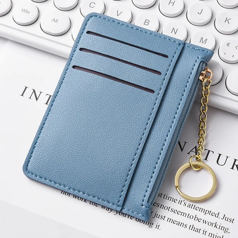 Dünne hellblaue Kartenwallet mit Reißverschluss auf einer weißen Tastatur.