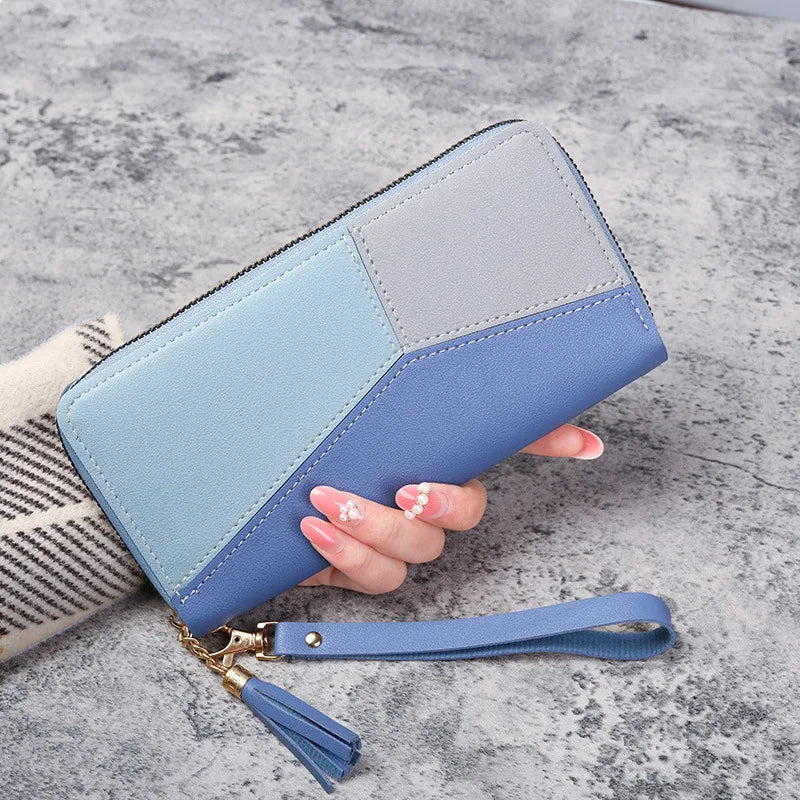 A light blue and lavender checkered fashion zipper wallet held in a woman's hand on a gray surface.