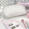 A white polka dot shell pencil case next to a pink cosmetic bag and a pink pencil.