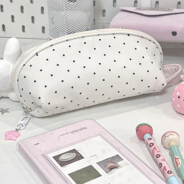 Une trousse à crayon en coquillage à pois blancs à côté d'un sac de maquillage rose et d'un crayon rose.