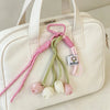 A cream-colored bag features a pink and green tulip flower charm keychain attached to the strap.