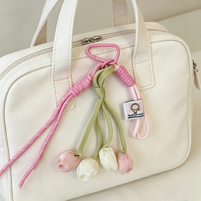 A cream-colored bag features a pink and green tulip flower charm keychain attached to the strap.