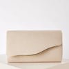 A beige velvet evening clutch with a gold-toned detachable shoulder strap resting on a white surface.