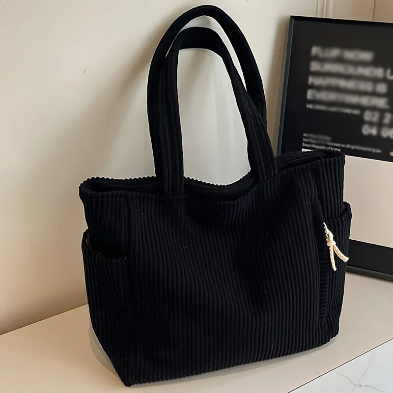 A black corduroy casual handbag with a drawstring closure and gold-colored tassel detail.