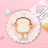 A cute cartoon toast bread plush toy shaped like a coin purse is displayed on a pink plate.