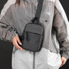 A woman is wearing a gray and white jacket with a black chest bag attached to her shoulder.
