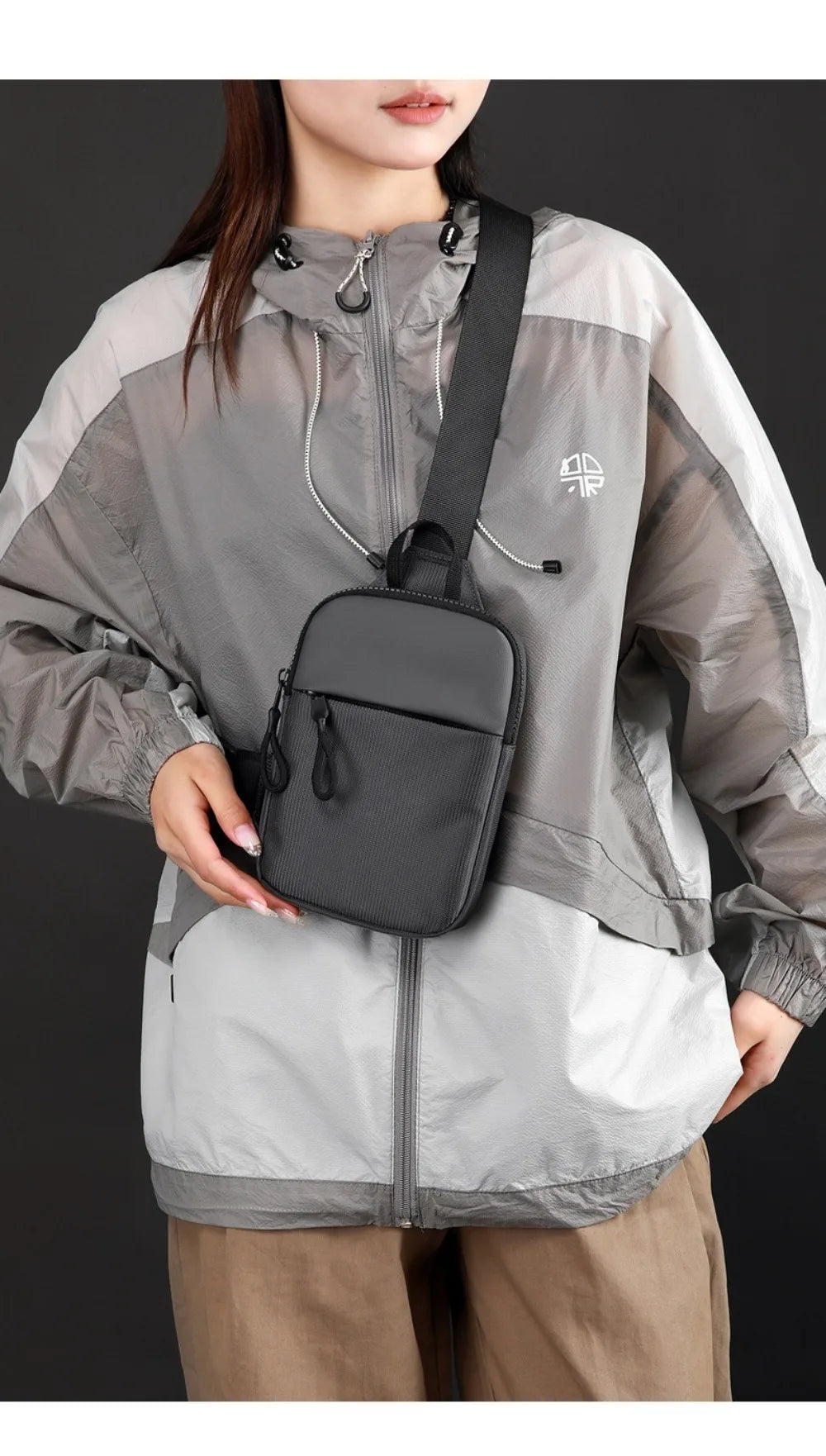 A woman is wearing a gray and white jacket with a black chest bag attached to her shoulder.