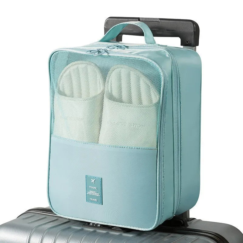 A light blue portable luggage shoe organizer bag with mesh pockets resting on a silver suitcase.