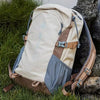 A beige and brown durable 80L waterproof hiking backpack resting on a dark rock amidst green grass.