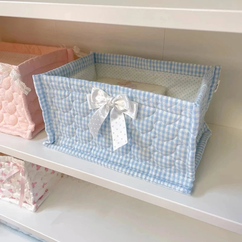 Light blue quilted cotton storage basket with a white bow on a white shelf