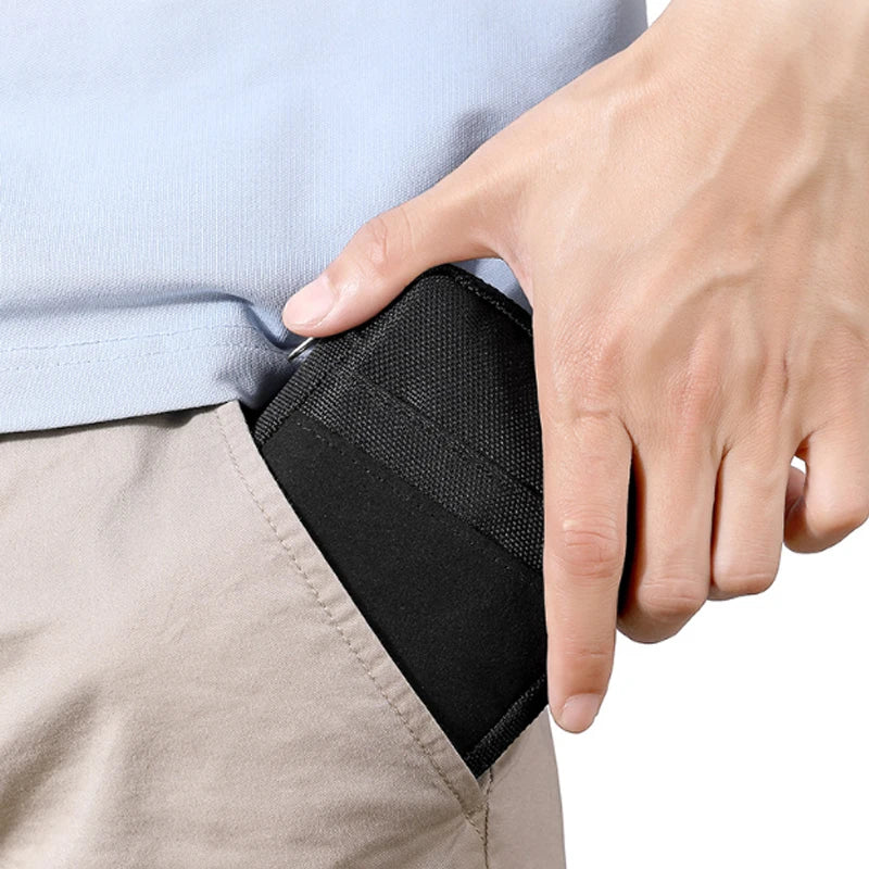 A hand is holding a black organizer pouch for outdoor gear against a light blue shirt and tan pants.