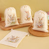 A set of six light beige drawstring gift bags featuring watercolor illustrations of rabbits and flowers.