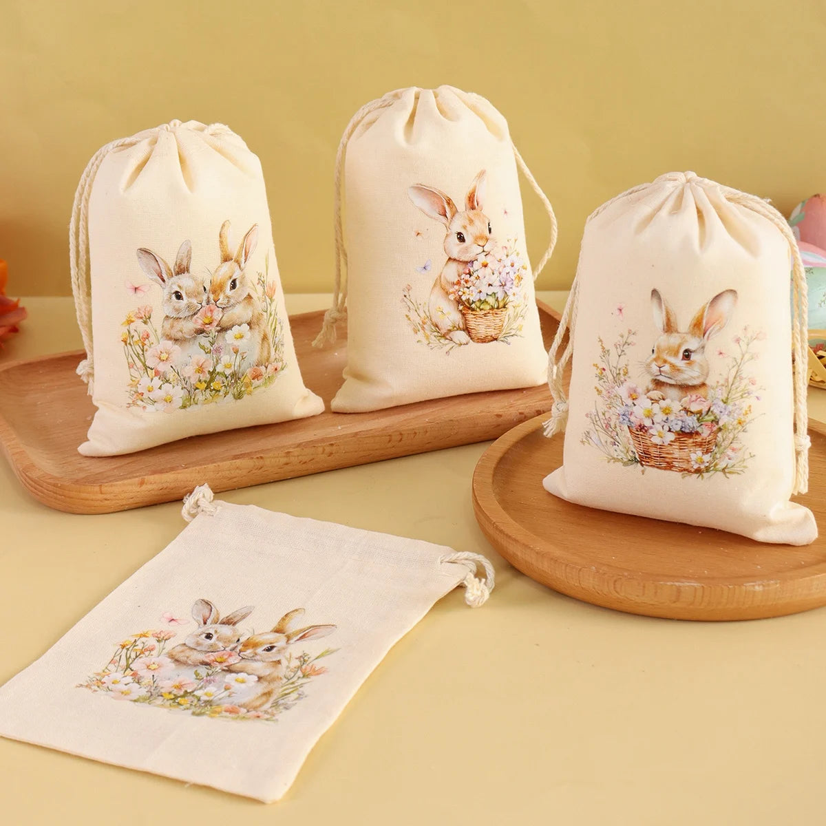 A set of six light beige drawstring gift bags featuring watercolor illustrations of rabbits and flowers.