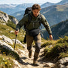 A man wearing a tactical concealed carry waist pack hikes on a rocky mountain trail.