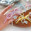 A hand holds a string of pink and purple pearl beaded bowknot keychains on a wooden surface.