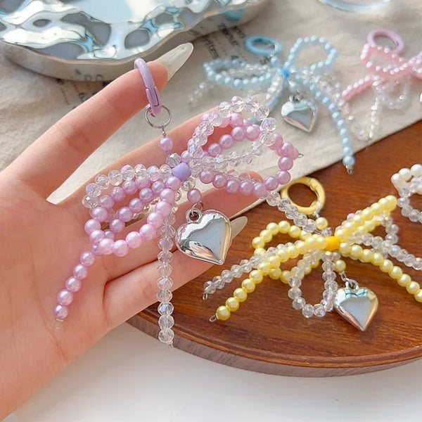 A hand holds a string of pink and purple pearl beaded bowknot keychains on a wooden surface.