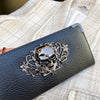 A black leather wallet with an ornate silver skull design resting on a light-colored fabric.