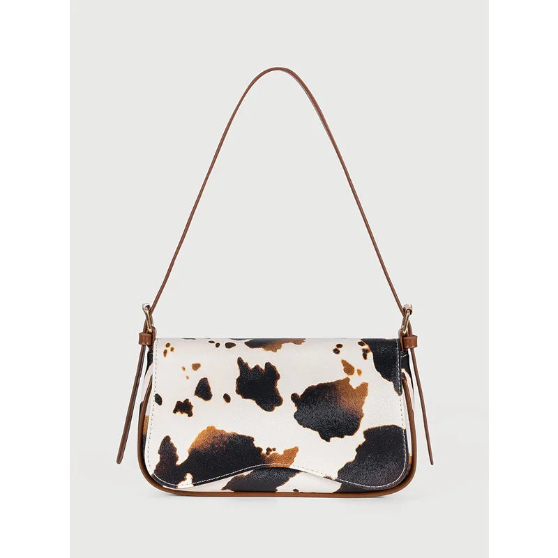 A beige and black cow print single shoulder bag with a brown adjustable strap.