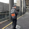 A person wearing a black padded jacket and a vintage Y2K telephone backpack walks down an outdoor walkway.