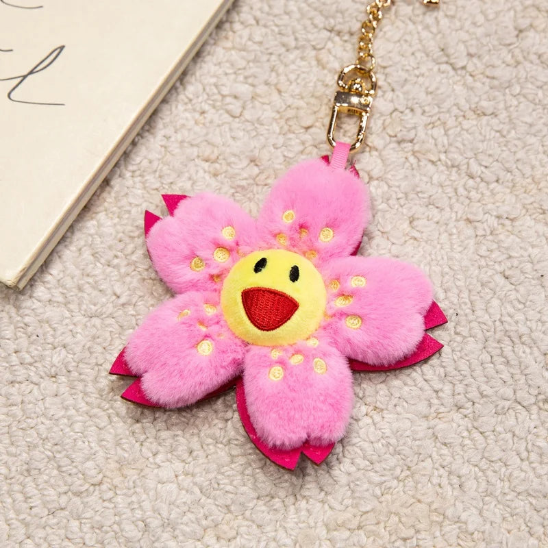 A pink fluffy sunflower plush keychain with a yellow center and gold chain.