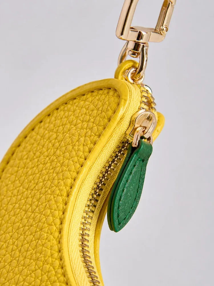 A yellow fruit-shaped PU leather coin purse keychain with a gold-toned clasp and a green fabric tag.