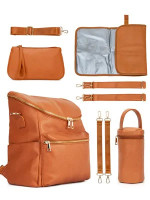 A tan leather diaper bag backpack with a matching fabric pouch and accessories.