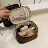 A brown faux suede cosmetic bag is open, revealing a netted interior and several makeup products.