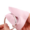 A hand holds a silver ring next to a pink polishing cloth, demonstrating a polishing cloth set for jewelry.