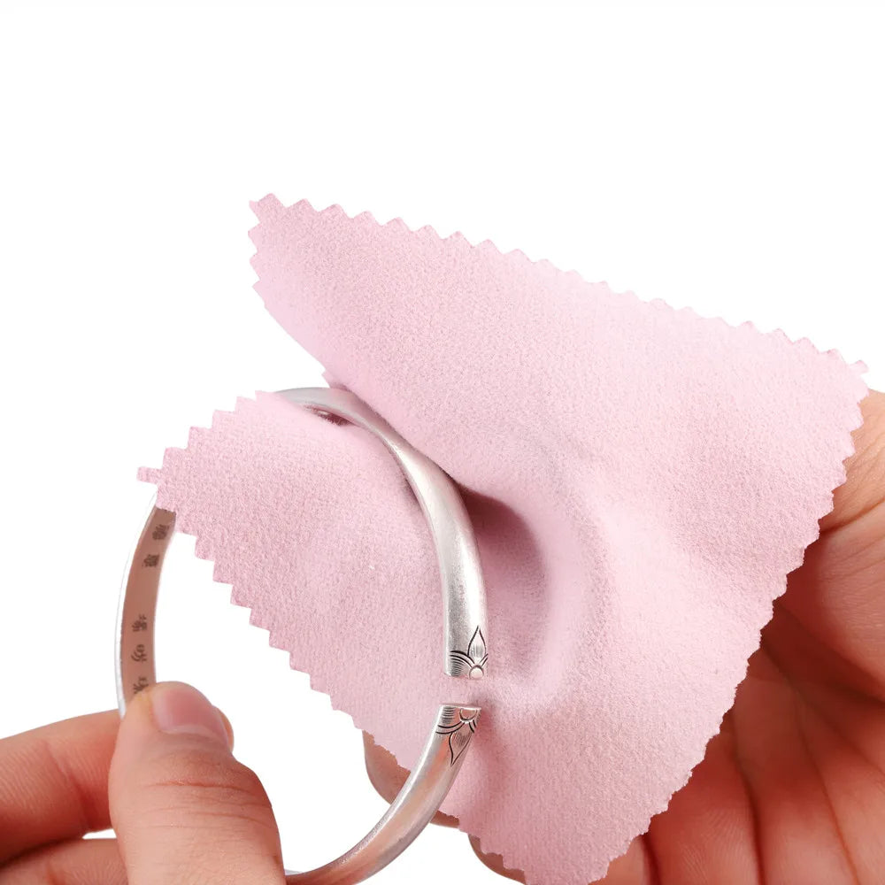 A hand holds a silver ring next to a pink polishing cloth, demonstrating a polishing cloth set for jewelry.