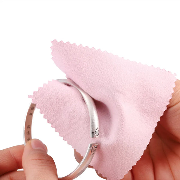 A hand holds a silver ring next to a pink polishing cloth, demonstrating a polishing cloth set for jewelry.