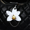 A white phalaenopsis orchid flower keychain hangs from a black leather handbag.