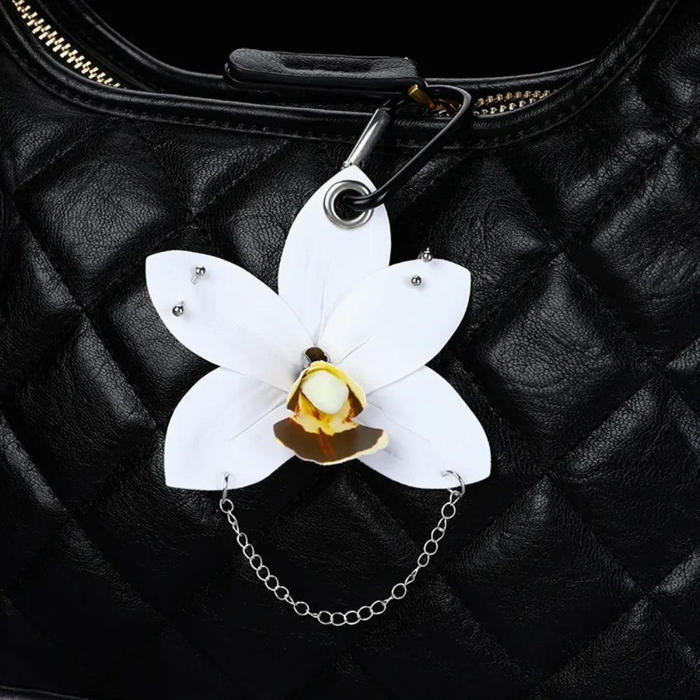 A white phalaenopsis orchid flower keychain hangs from a black leather handbag.