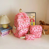 A pink nylon travel backpack set featuring a cute bow print, displayed next to a lamp and a framed picture.
