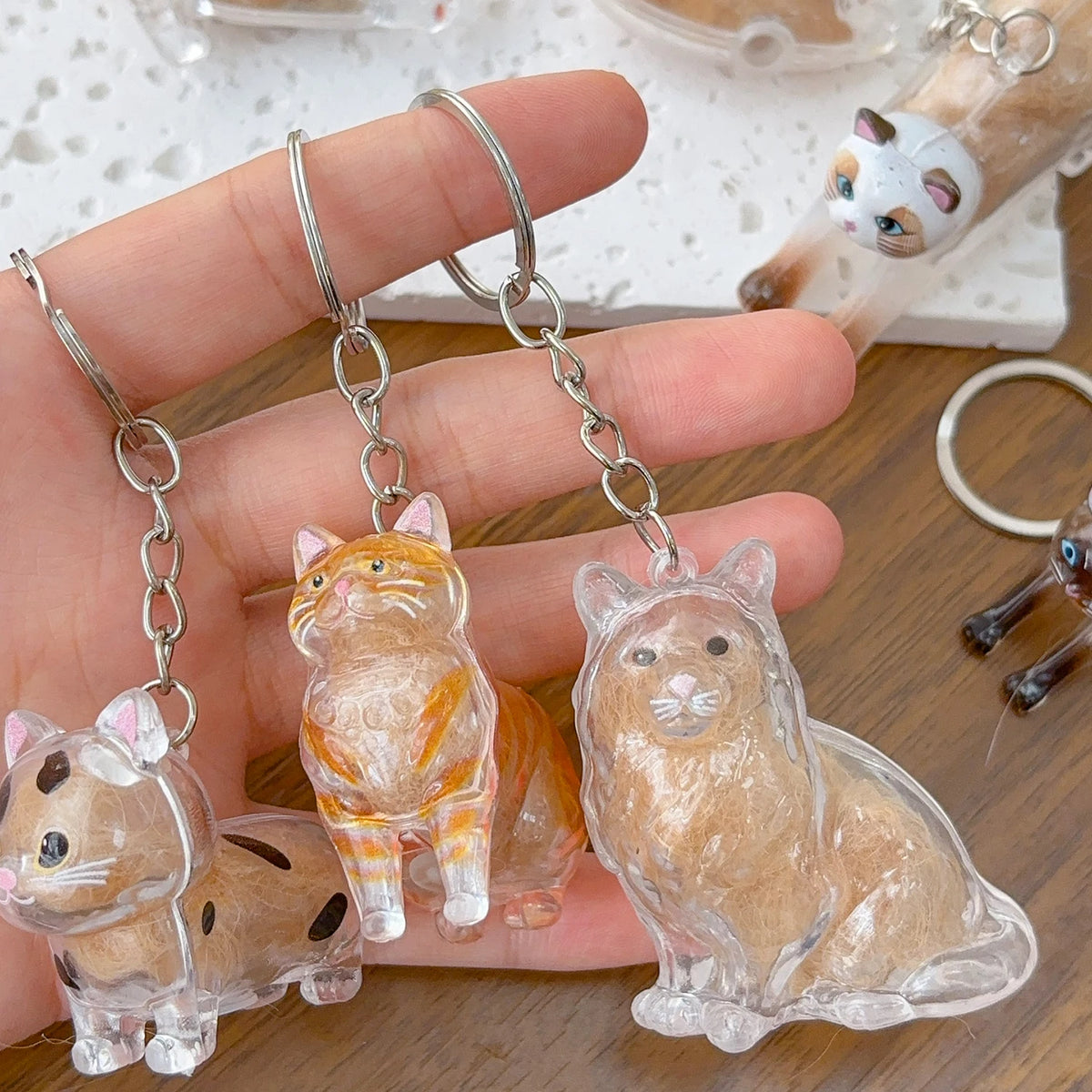 A hand holds a transparent cat fur keepsake keychain pendant featuring an orange tabby cat.