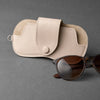 A beige PU leather storage case for eyeglasses resting next to a pair of brown sunglasses.