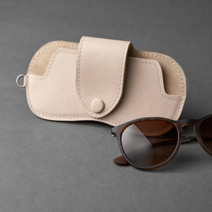 A beige PU leather storage case for eyeglasses resting next to a pair of brown sunglasses.