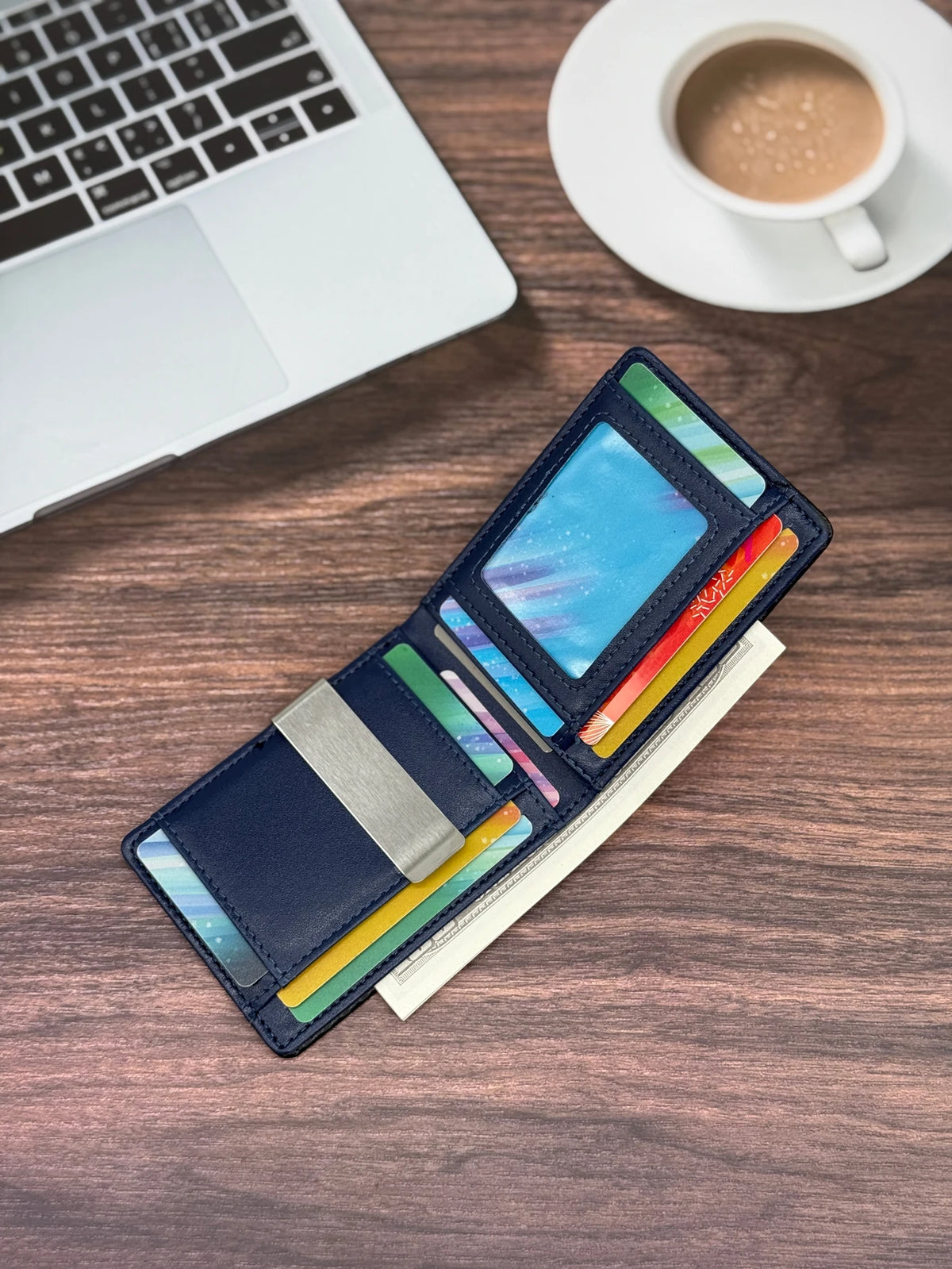 A dark blue men's carbon fiber microfiber wallet lying on a wooden surface next to a laptop and a coffee cup.