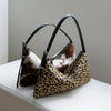 A black leather crossbody bag featuring a leopard print pattern and cowhide accents, resting on a white surface.
