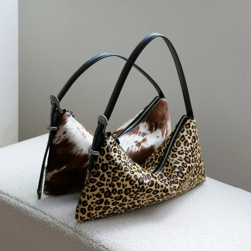A black leather crossbody bag featuring a leopard print pattern and cowhide accents, resting on a white surface.