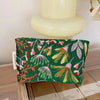 A dark green cosmetic pouch with floral embroidery rests on a light-colored ceramic stand.