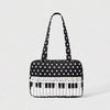 A black tote bag with white polka dots featuring a piano key trim and bow detail.